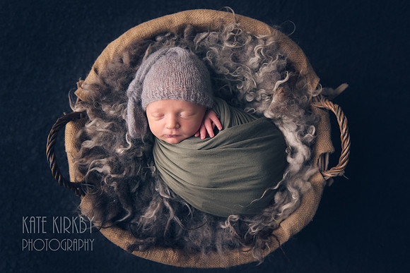 Swaddled newborn in basket on a fluffy rug